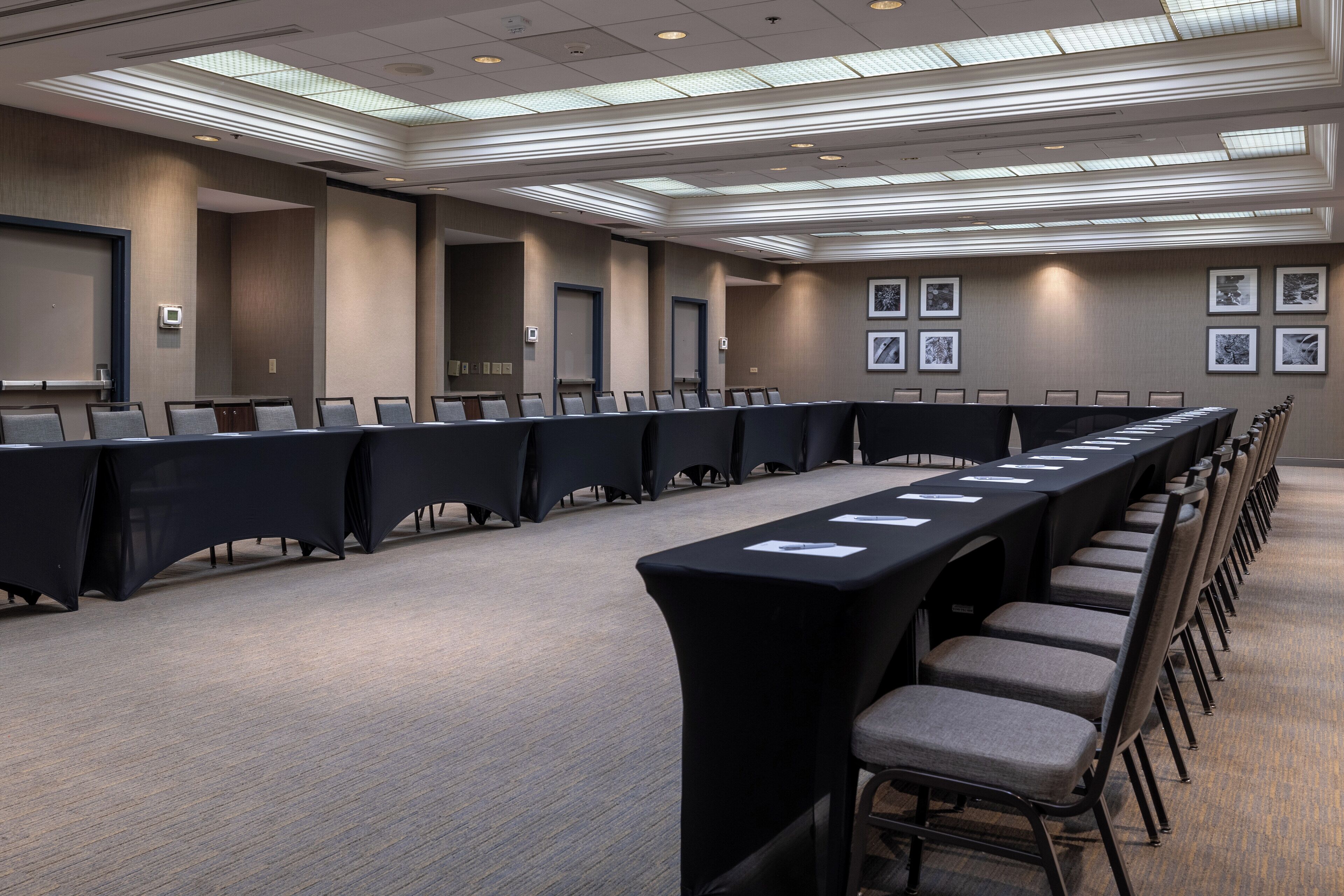 A conference room with long tables and chairs, a carpeted floor, and framed pictures on the walls.