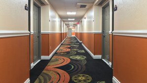 Un pasillo de hotel con alfombra de diseños circulares, paredes color beige y puertas con los números 114 y 117.