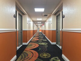 Un pasillo de hotel con alfombra de diseños circulares, paredes color beige y puertas con los números 114 y 117.