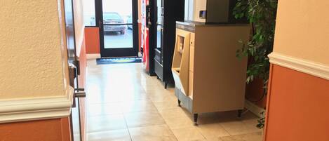 A hallway with a vending machine, a door leading outside, and a potted plant.