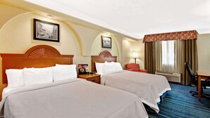 Habitación de hotel con dos camas, un escritorio, una silla y una ventana con cortinas.