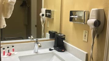 A hotel bathroom with a sink, mirror, towel rack, hair dryer, and a coffee maker.