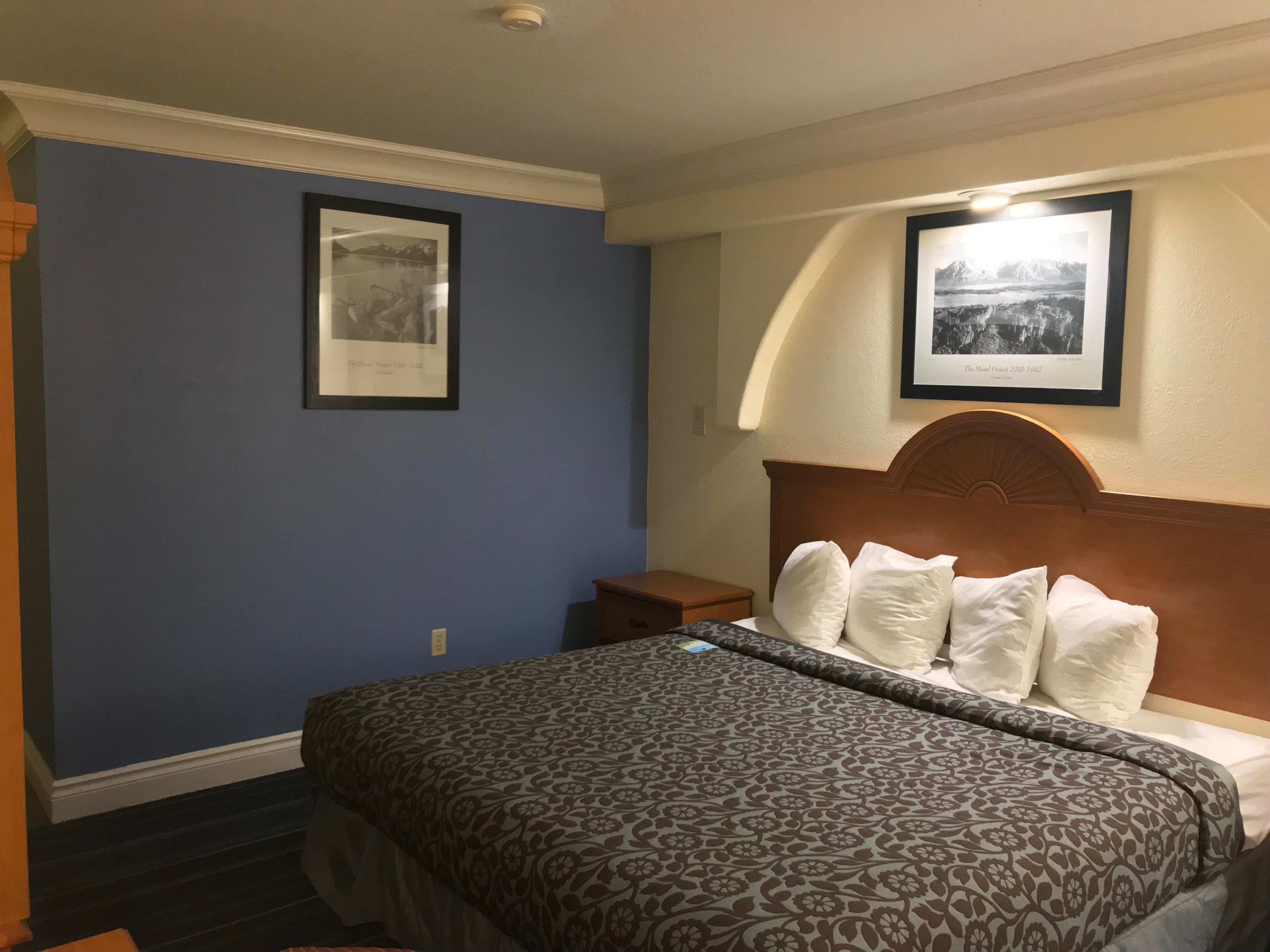 Ein Hotelzimmer mit einem Bett, einem Nachttisch und zwei gerahmten Bildern an der Wand.