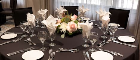 Une table de salle à manger ronde, dressée avec de l’argenterie, des assiettes blanches et des verres à vin, et agrémentée d’un arrangement floral au centre.