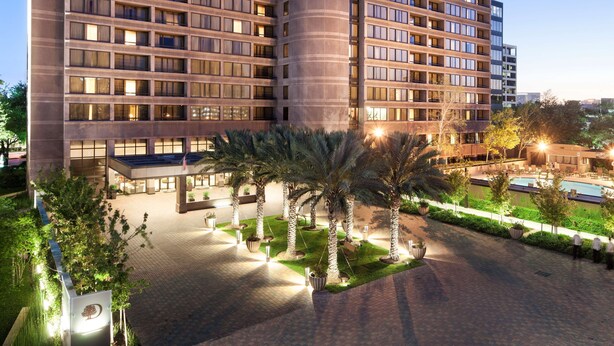 Un hotel moderno de altura, con un patio central con palmeras y una piscina.