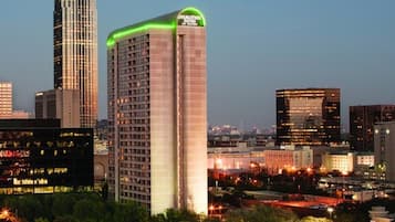 A cityscape at dusk with high-rise buildings, including a hotel with a distinctive green-lit top.