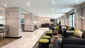Un vestíbulo espacioso con diseño moderno, que incluye una zona de estar con sofá y sillones, una mesa de centro, y un comedor con mesa y sillas.