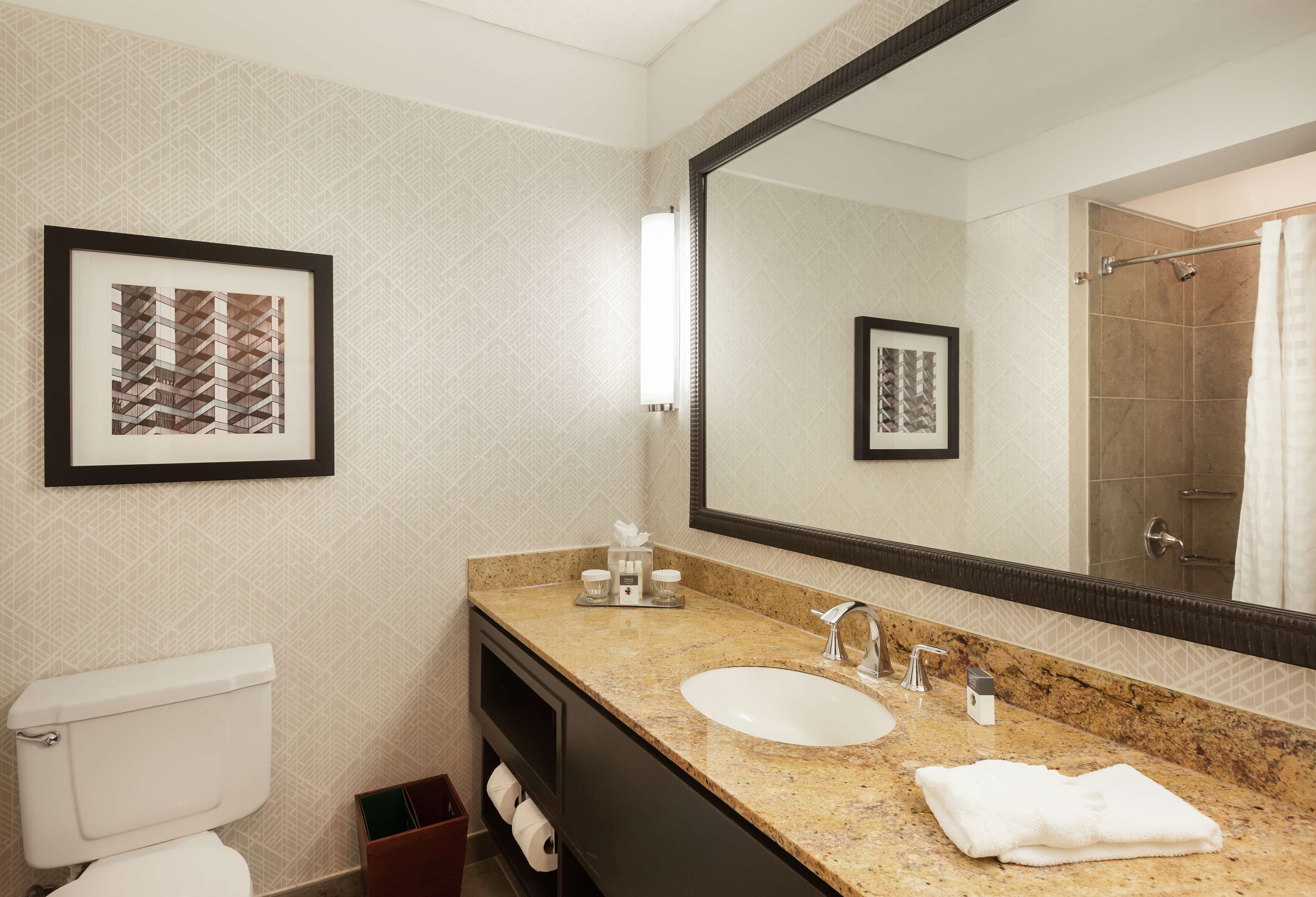 A bathroom with a toilet, sink, and mirror. There are framed pictures on the wall and a towel on the counter.