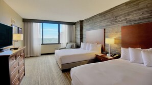 Habitación de hotel con dos camas, televisor, escritorio y ventana grande con vistas.