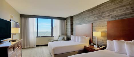 Habitación de hotel con dos camas, televisor, escritorio y ventana grande con vistas.