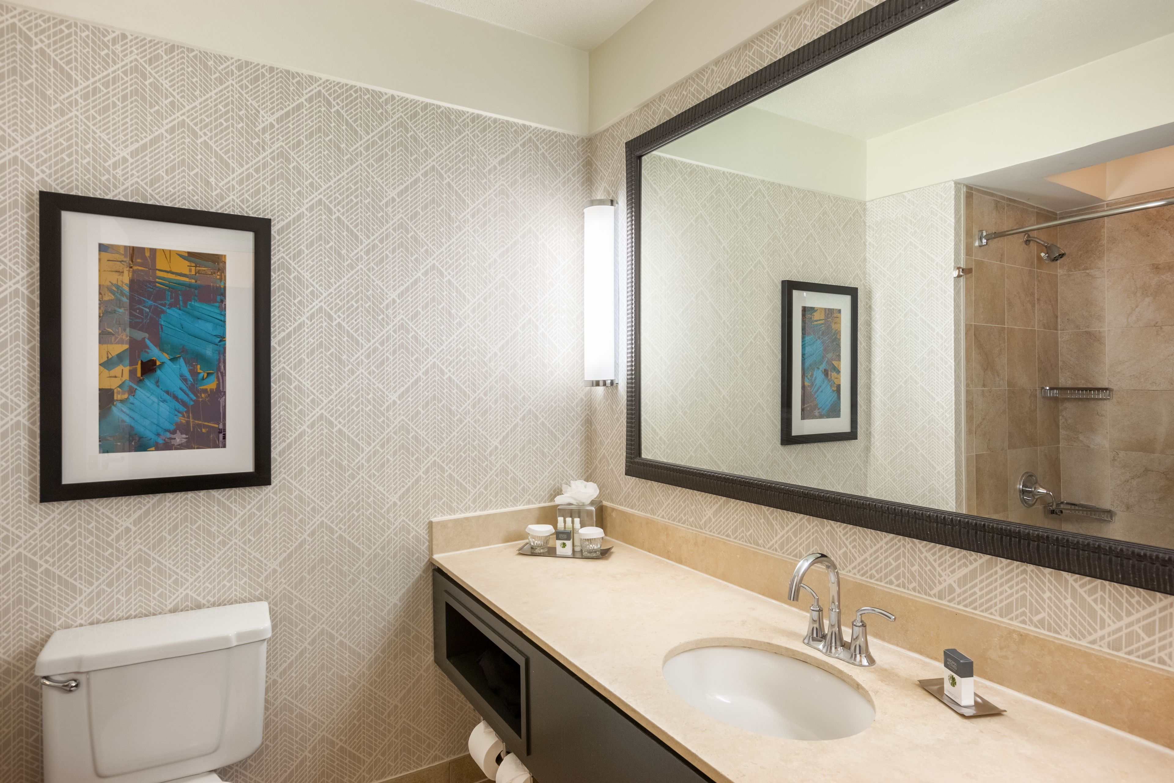 A modern bathroom with a large mirror, a sink, and a toilet. There are framed pictures on the wall and a towel rack.