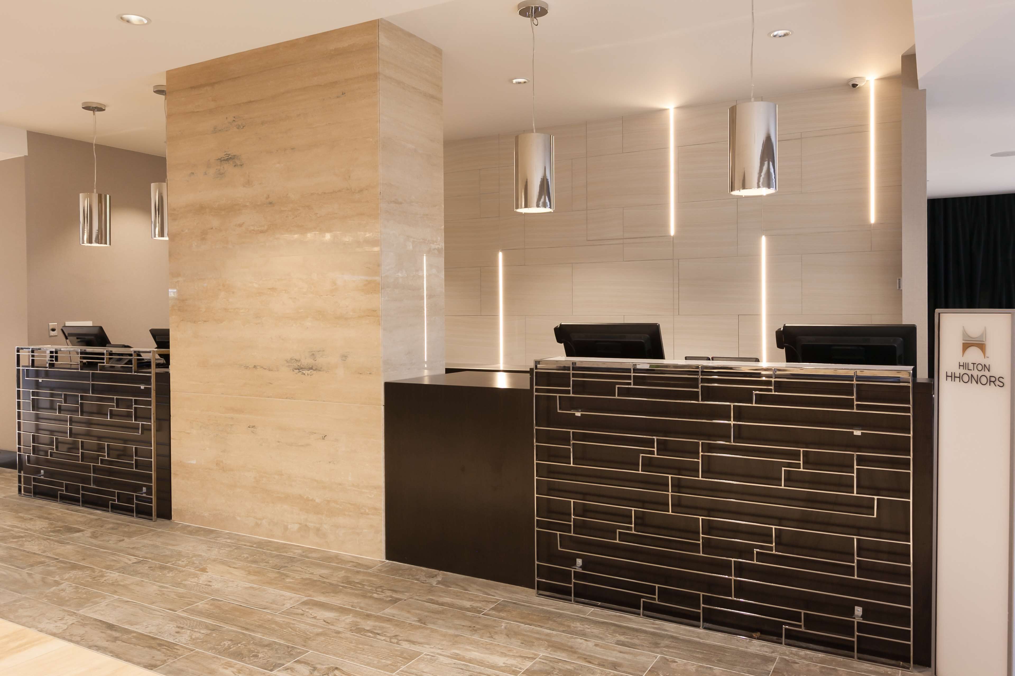 A modern hotel reception area with a marble column, a reception desk with a geometric design, and pendant lighting.