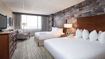 A hotel room with two beds, a desk, a TV, and a large window with curtains.