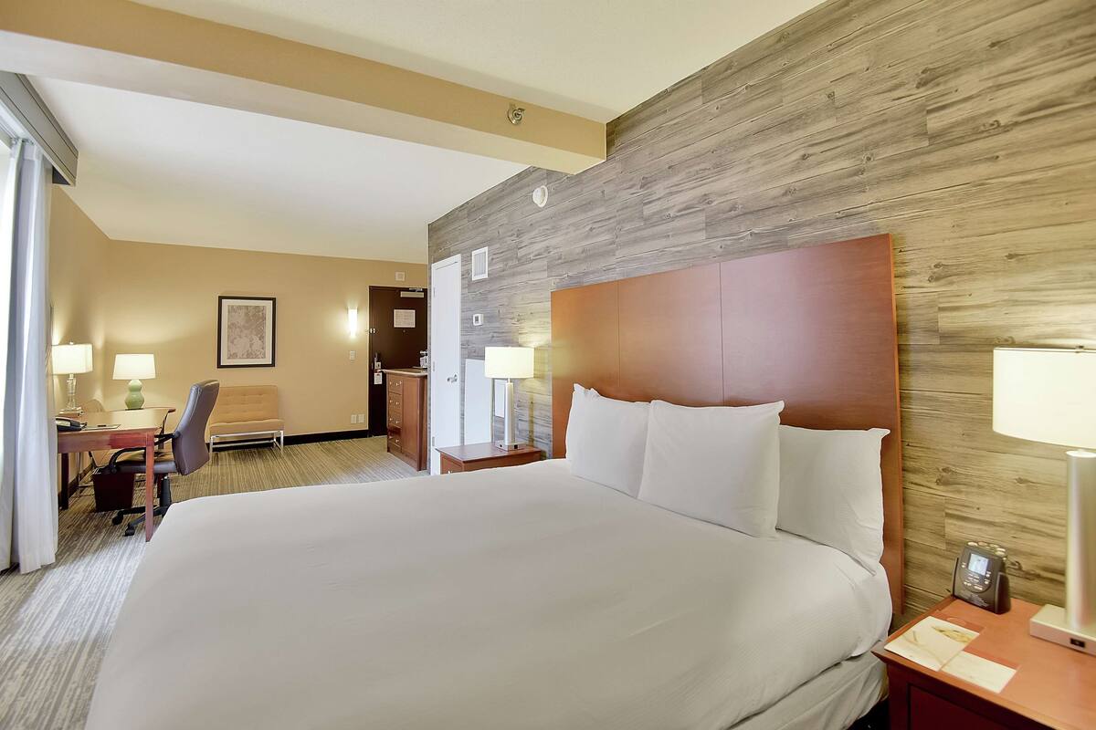 Habitación de hotel con una cama grande, un escritorio con silla, una lámpara y un revestimiento de madera.