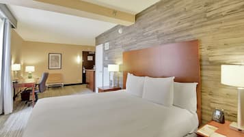 A hotel room with a large bed, a desk with a chair, a lamp, and a wooden accent wall.