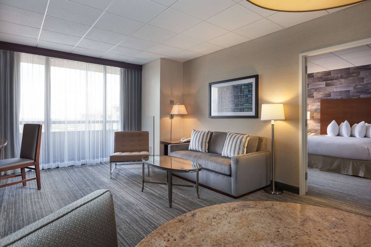 Una habitación de hotel con sofá, sillón, mesa de centro y cama con cabecero.