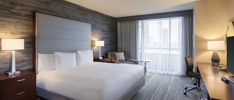 A hotel room with a large bed, a desk, a chair, a small table, and a window with curtains.
