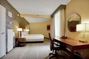 Quarto de hotel com cama, escrivaninha, cadeira e um espelho grande.