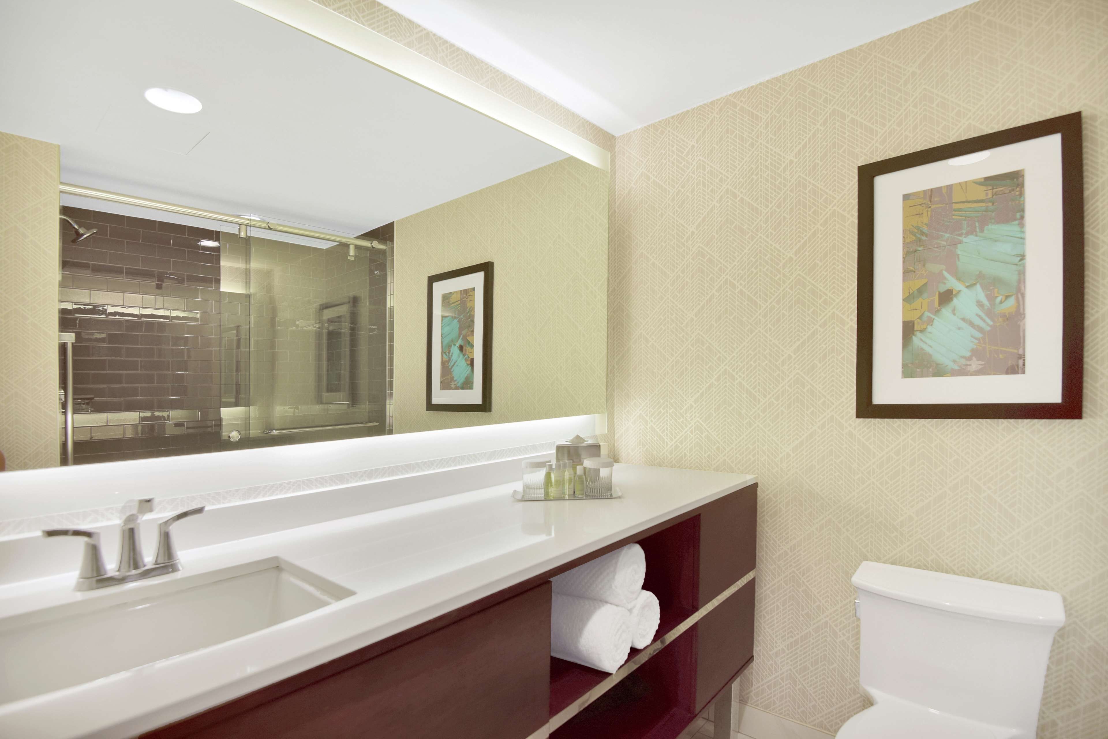 A modern bathroom with a large mirror, dual sinks, a toilet, and a towel rack.