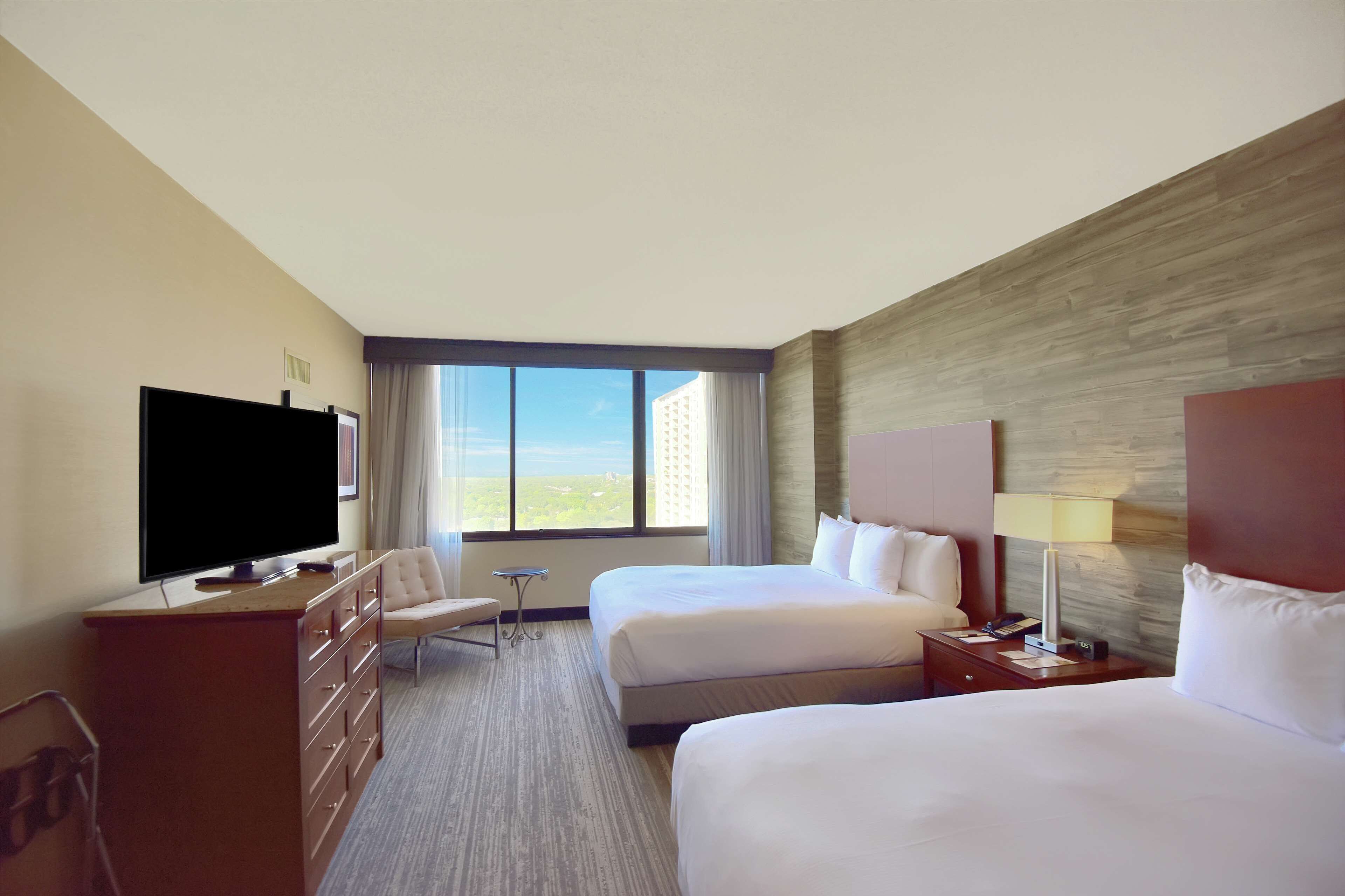 A hotel room with two beds, a TV, a desk, a chair, and a window with a view.
