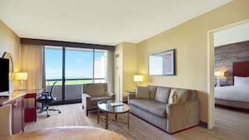 Una habitación de hotel con cama, sofá, escritorio, silla, mesita y un amplio ventanal con vistas a la ciudad.