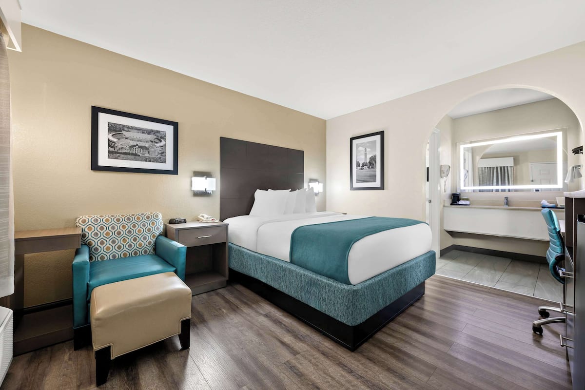 A hotel room with a bed, a desk, a chair, a nightstand, and a mirror.