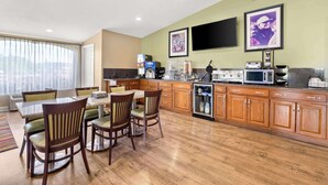 Une cuisine moderne avec des meubles en bois, un coin repas avec quatre chaises, un four encastré et une grande fenêtre avec des rideaux.