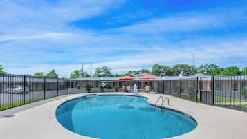 A swimming pool with a black fence, a red umbrella, and a building with a blue roof in the background.