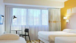 Une chambre d’hôtel avec deux lits, une petite table, une chaise et une fenêtre avec des rideaux.
