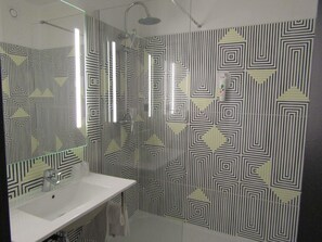 Un baño con un lavamanos blanco, un espejo y una ducha con un revestimiento de pared de diseño geométrico.