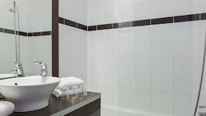 Une salle de bain avec un lavabo blanc, un miroir, une serviette et une douche.