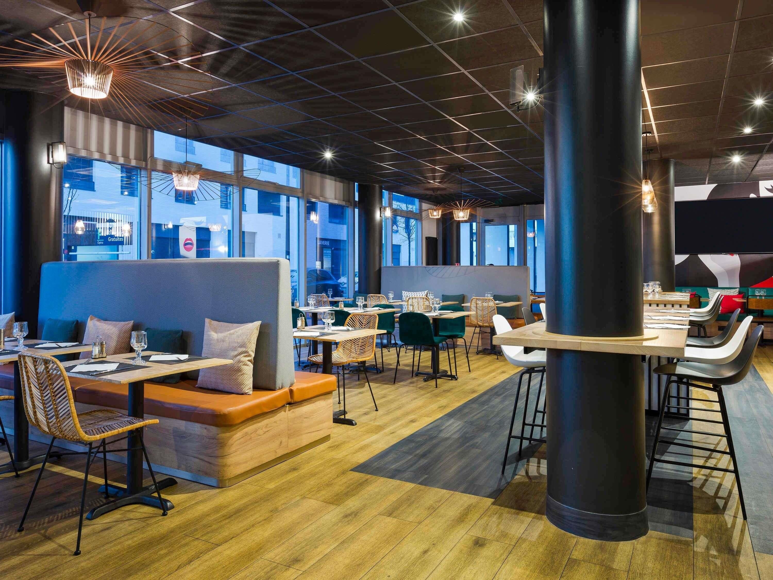 A modern restaurant interior with high ceilings, large windows, and a mix of seating arrangements including booths and tables.