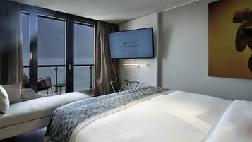 Habitación de hotel con una cama grande, televisión, vista al mar y balcón con una silla.