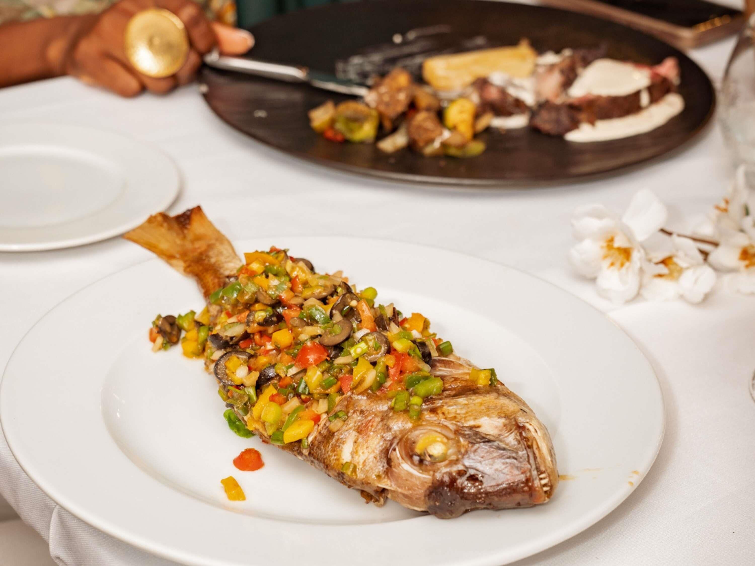 Un plato con un pescado cocinado, cubierto con una mezcla de vegetales de colores.