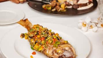 Un plato con un pescado cocinado, cubierto con una mezcla de vegetales de colores.