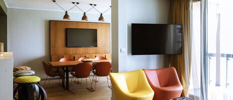 Una sala de estar moderna con comedor, un televisor de pantalla plana y un amplio ventanal con cortinas.