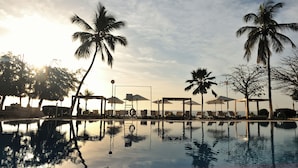 A poolside area with lounge chairs and umbrellas, palm trees, and a clear sky. - Pullman Dakar Teranga (Dakar)
