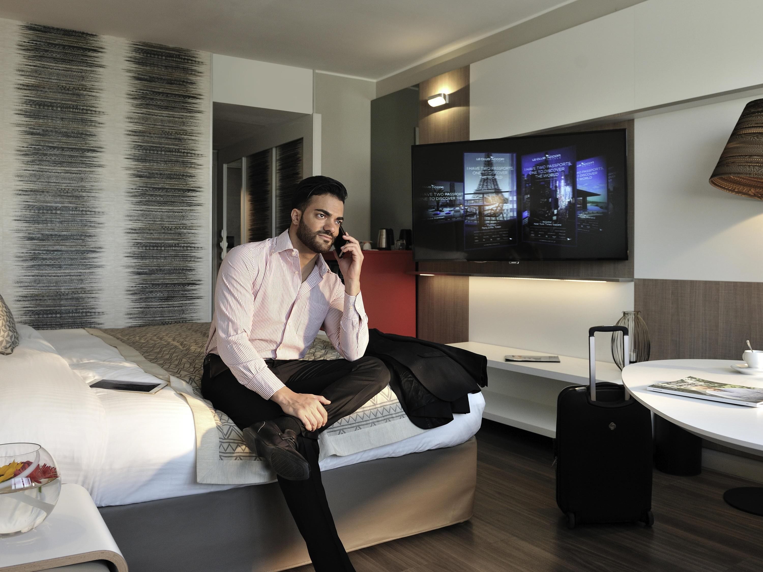 Une chambre d’hôtel moderne équipée d’un lit, d’un téléviseur fixé au mur, d’une petite table et d’une valise.