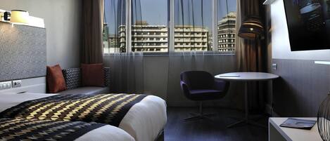 Habitación de hotel con cama, una silla, mesita, televisor y ventana con vista a la ciudad.