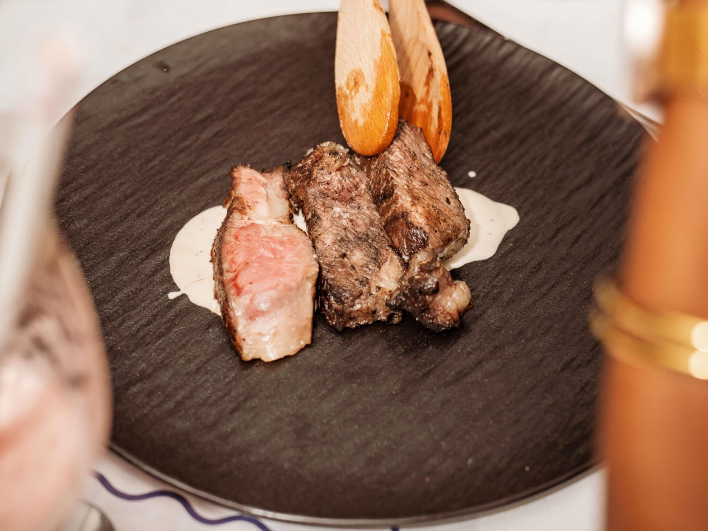 Une assiette avec un steak et une sauce, une spatule en bois et une assiette foncée à texture marquée.