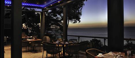 An outdoor dining area with tables and chairs, overlooking a body of water.