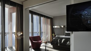 A modern hotel room with a large bed, a TV, a desk with a chair, and large windows with curtains. - Pullman Dakar Teranga (Dakar)