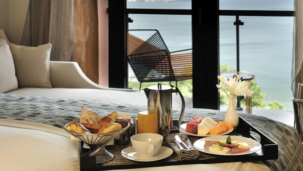 A bed with a tray of breakfast items, a vase of flowers, and a view of the sea. - Pullman Dakar Teranga (Dakar)