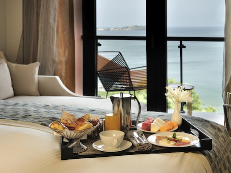 Un lit avec un plateau de petit-déjeuner, un vase de fleurs et une vue sur la mer.. Pullman Dakar Teranga