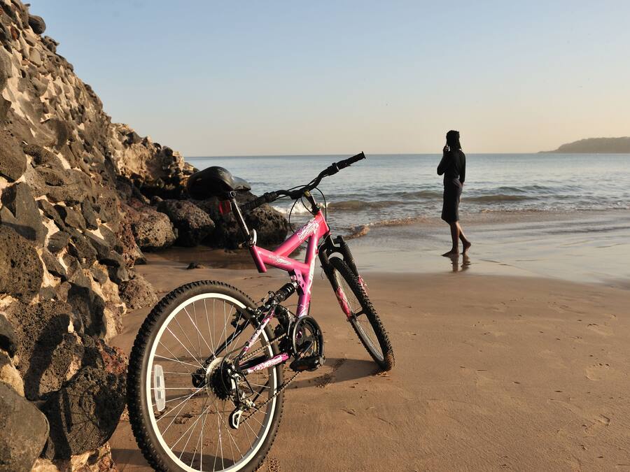 Een roze mountainbike geparkeerd op een zanderig strand, met een rotsachtige klif op de achtergrond.