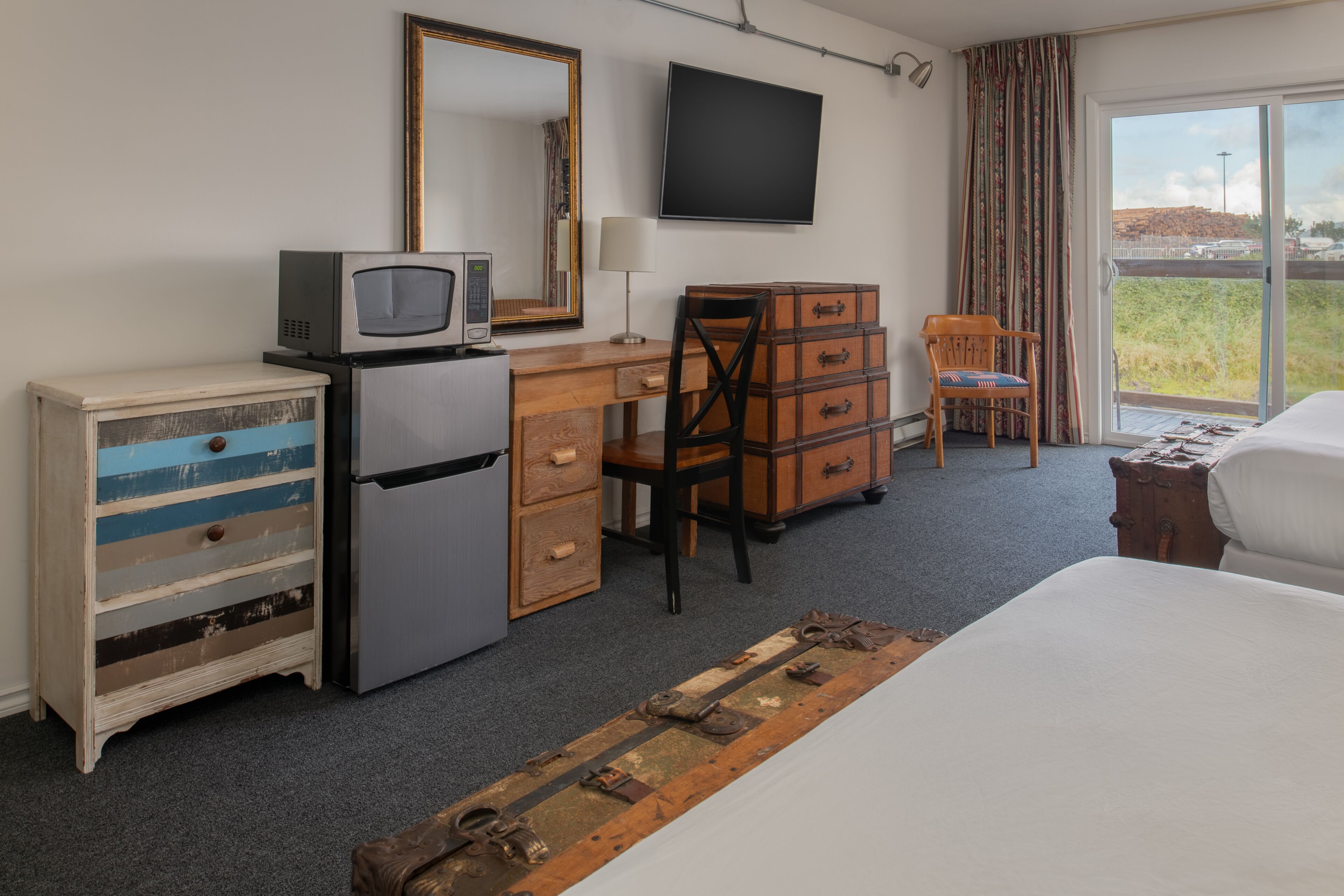 A hotel room with a bed, a desk with a computer, a television, a dresser, and a chair.