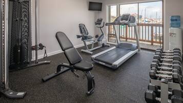 Un gimnasio con máquinas de cardio, bancos de pesas y mancuernas.