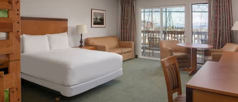 A hotel room with a large bed, a dining table, and a balcony with a view of a bridge and cityscape.