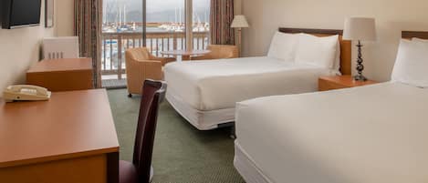A hotel room with two beds, a desk, a chair, a table, and a view of the marina.