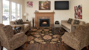 A living room with two patterned armchairs, a sofa, a fireplace, and a TV mounted on the wall.